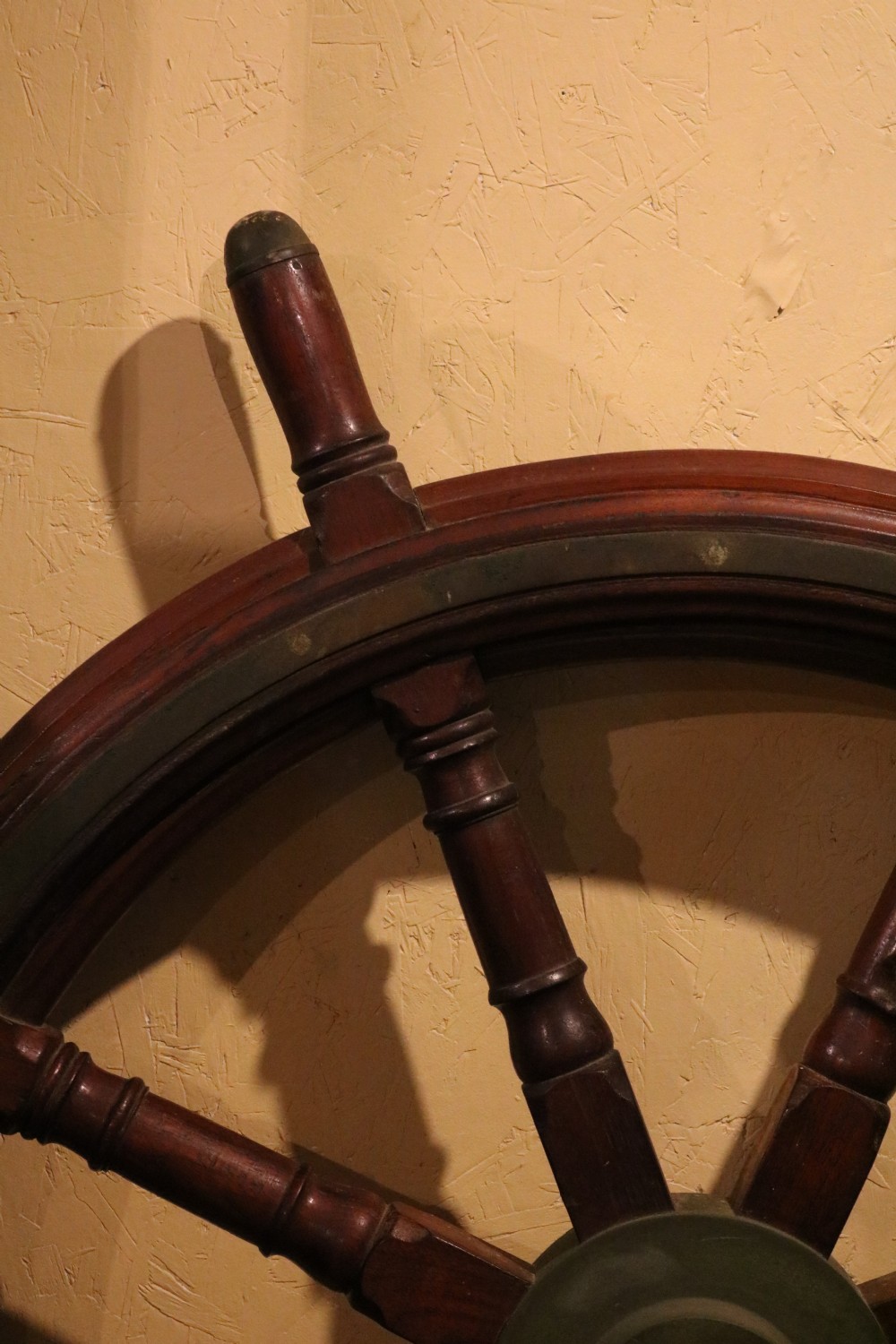A Victorian wooden ships wheel featuring eight turned spokes, a central brass boss, and outer brass rim reinforcement. View IX