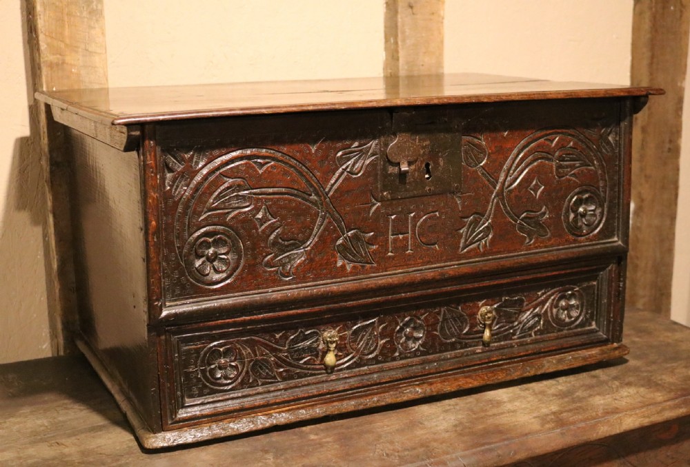 A 17th-century dark oak carved table box featuring scrollwork leaf motifs, carved initials HC, an iron lockplate, and a lower drawer. View V