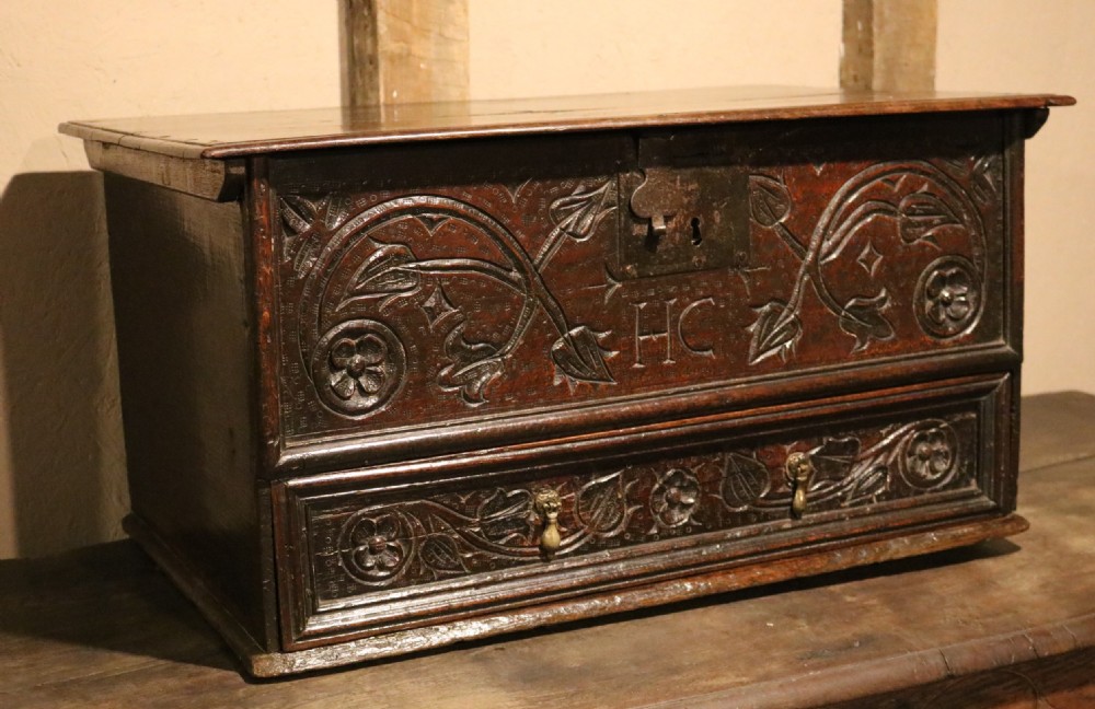 A 17th-century dark oak carved table box featuring scrollwork leaf motifs, carved initials HC, an iron lockplate, and a lower drawer. View VIII