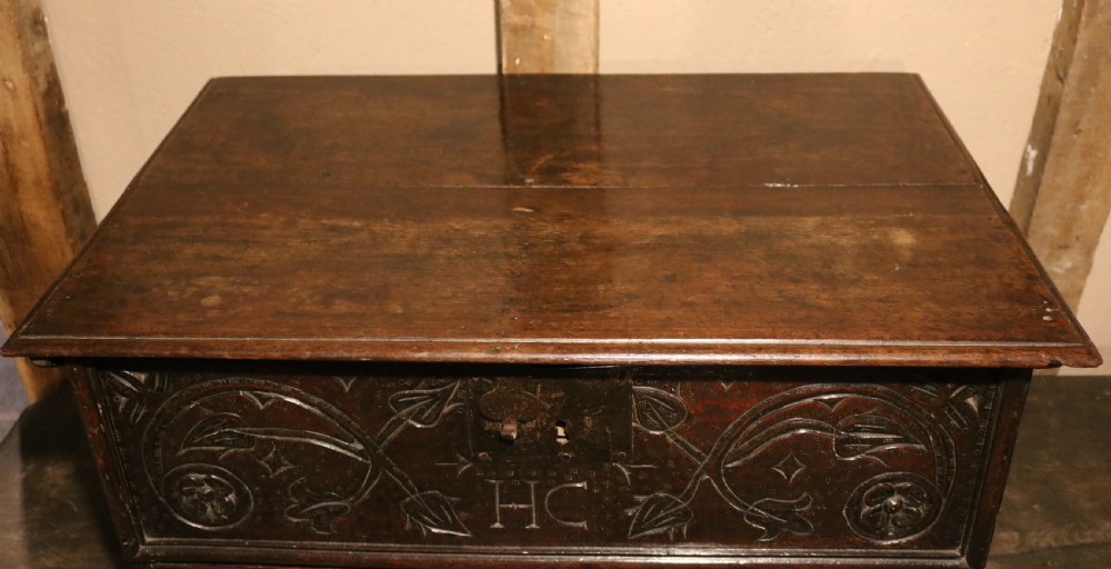 A 17th-century dark oak carved table box featuring scrollwork leaf motifs, carved initials HC, an iron lockplate, and a lower drawer. View XI