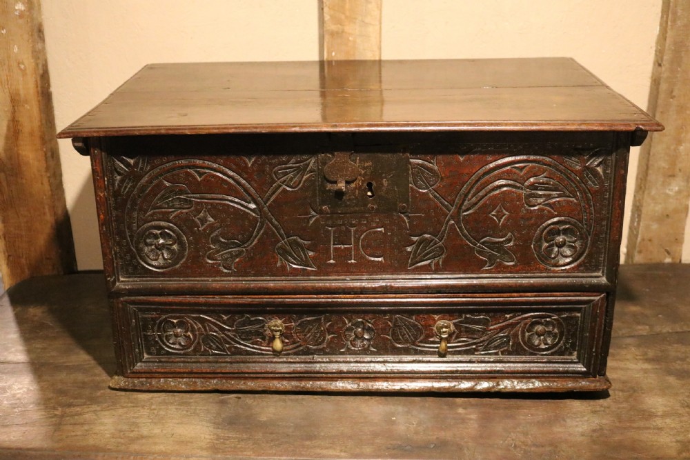 A 17th-century dark oak carved table box featuring scrollwork leaf motifs, carved initials HC, an iron lockplate, and a lower drawer. View XIII