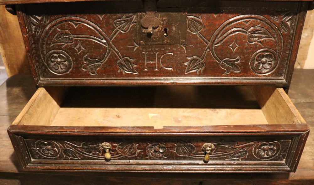 A 17th-century dark oak carved table box featuring scrollwork leaf motifs, carved initials HC, an iron lockplate, and a lower drawer. View XIV
