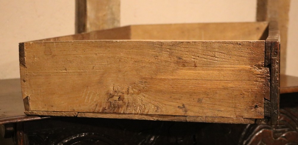 A 17th-century dark oak carved table box featuring scrollwork leaf motifs, carved initials HC, an iron lockplate, and a lower drawer. View XV
