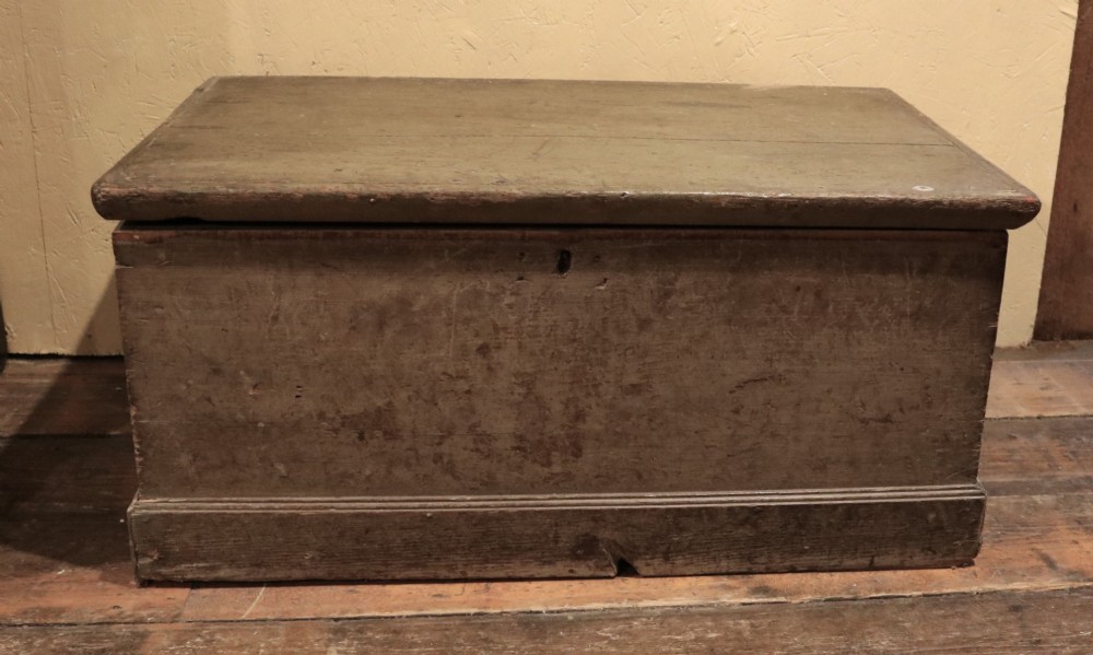 A small 19th-century Welsh painted pine artisan chest with a distressed grey-green finish, hinged rectangular lid, and moulded plinth base.