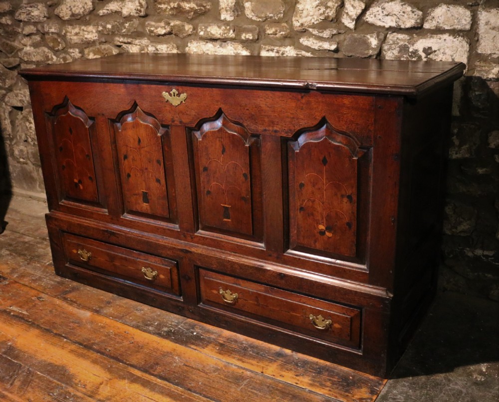 An 18th-century dark oak Welsh coffer featuring four arched inlaid panels above two drawers with brass handles.