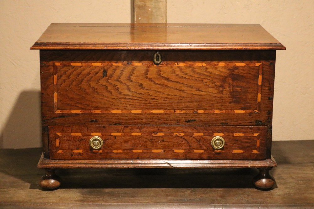 An 18th-century Welsh oak coffer bach featuring geometric inlay, a single lower drawer with brass handles, and turned bun feet.
