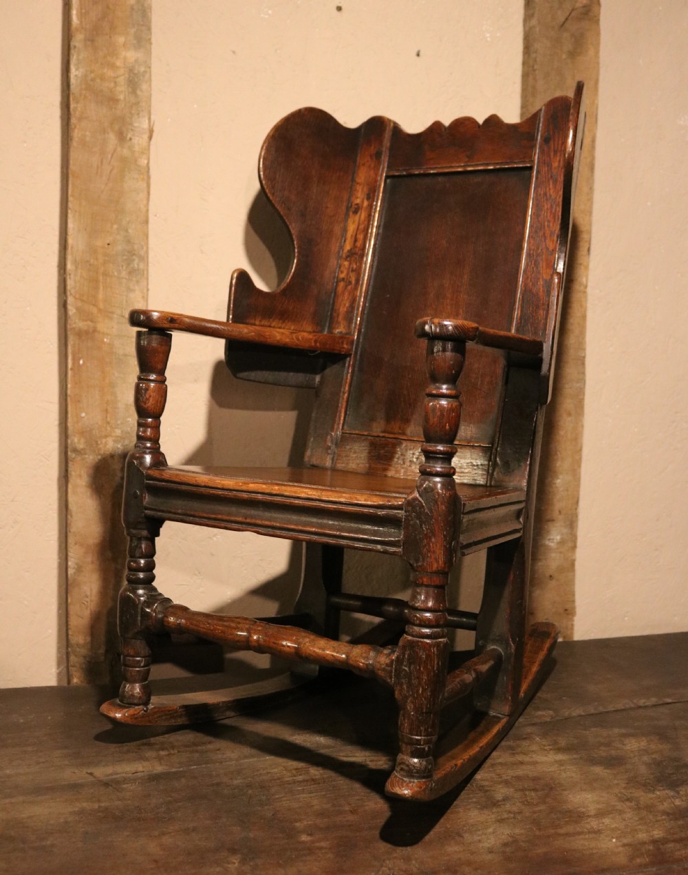 An antique dark oak childs lambing rocking chair featuring shaped winged sides, a panelled backrest, turned front supports, and curved wooden rockers. View III