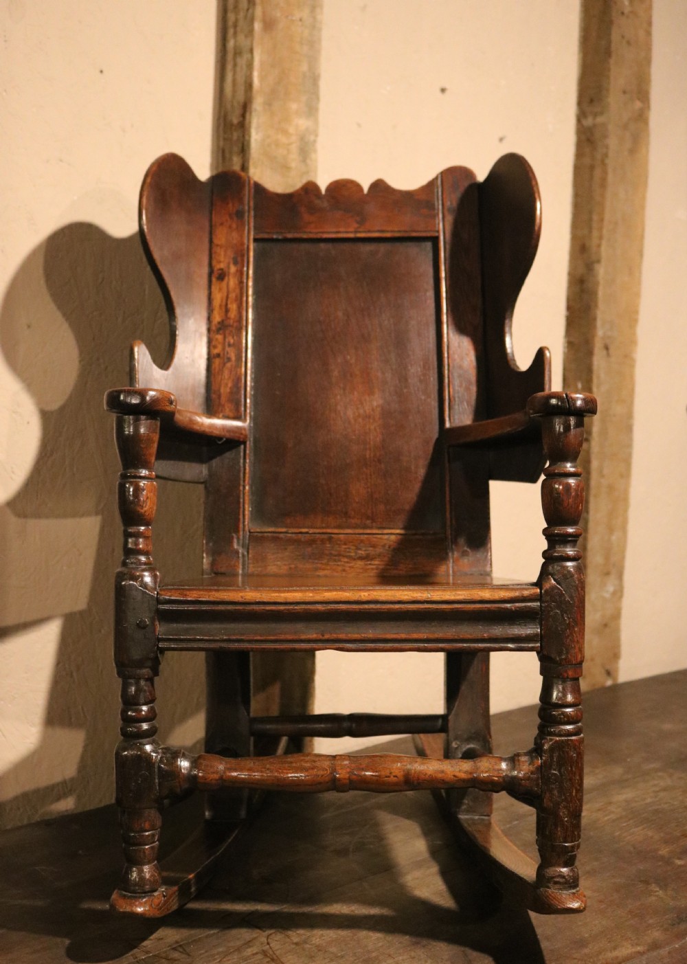 An antique dark oak childs lambing rocking chair featuring shaped winged sides, a panelled backrest, turned front supports, and curved wooden rockers. View V