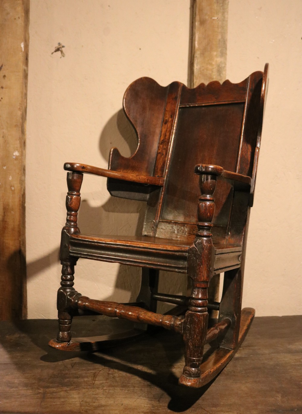 An antique dark oak childs lambing rocking chair featuring shaped winged sides, a panelled backrest, turned front supports, and curved wooden rockers. View VI