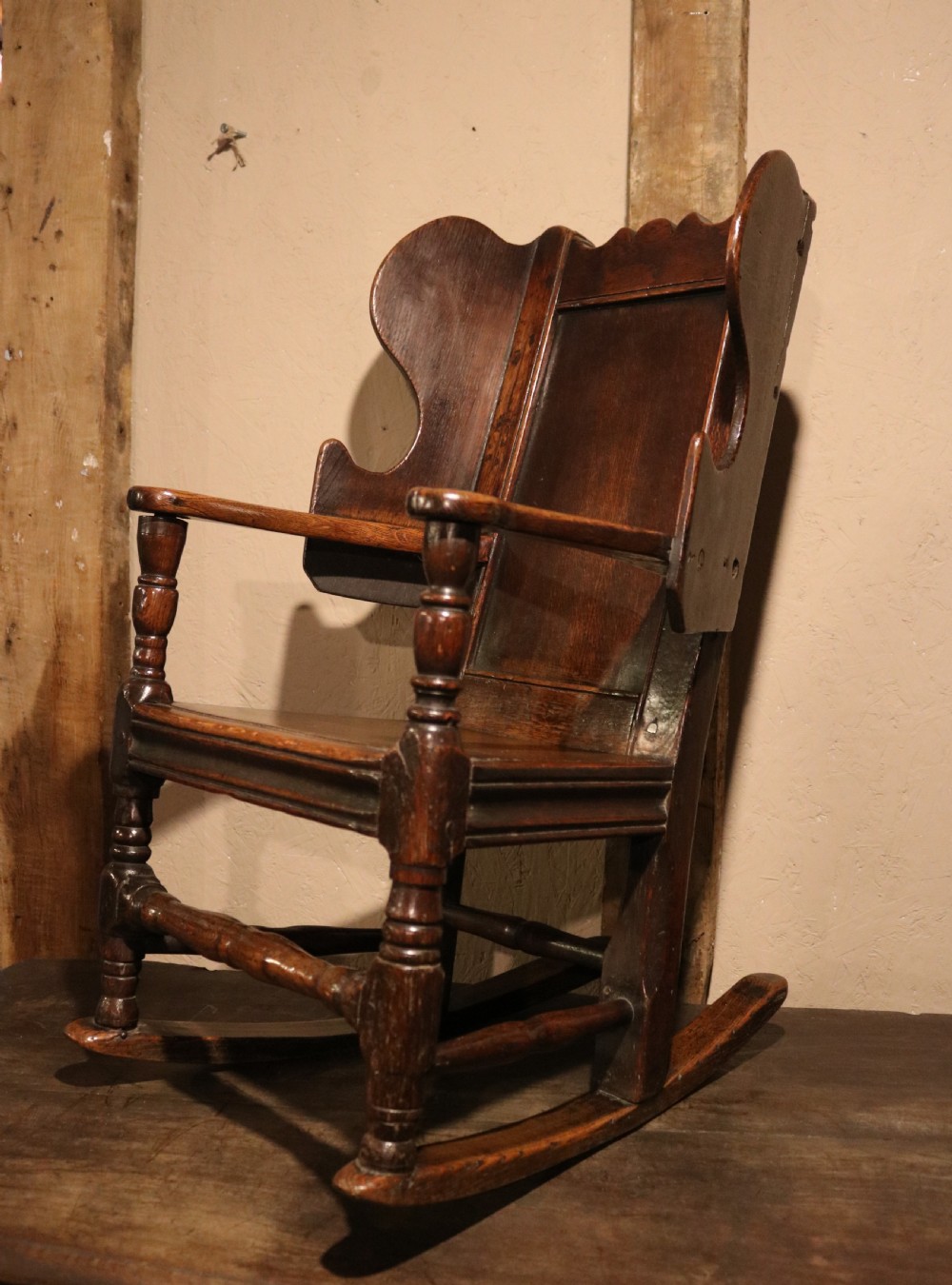 An antique dark oak childs lambing rocking chair featuring shaped winged sides, a panelled backrest, turned front supports, and curved wooden rockers. View VII
