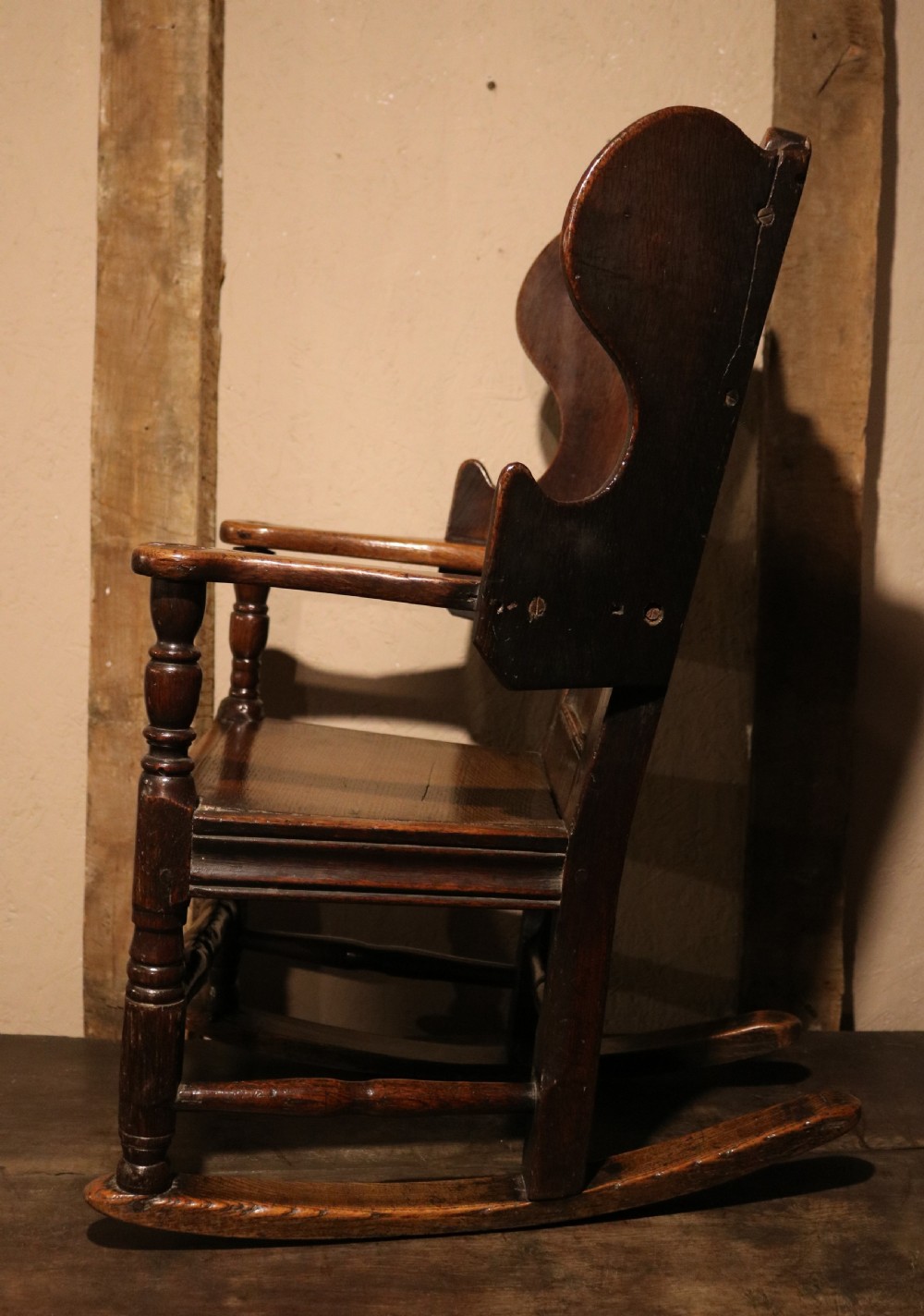 An antique dark oak childs lambing rocking chair featuring shaped winged sides, a panelled backrest, turned front supports, and curved wooden rockers. View VIII