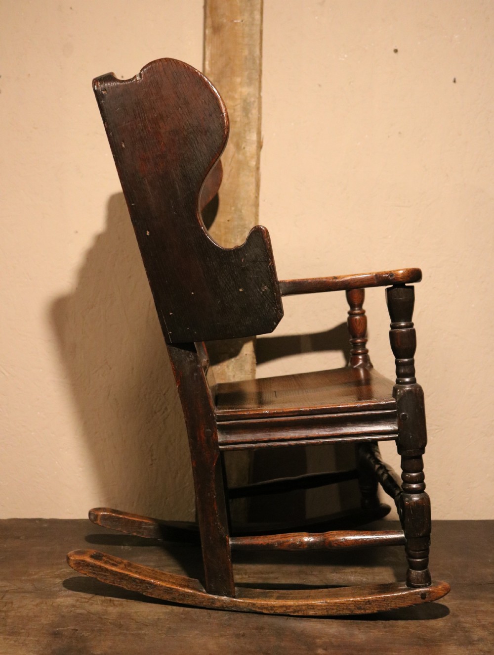 An antique dark oak childs lambing rocking chair featuring shaped winged sides, a panelled backrest, turned front supports, and curved wooden rockers. View IX