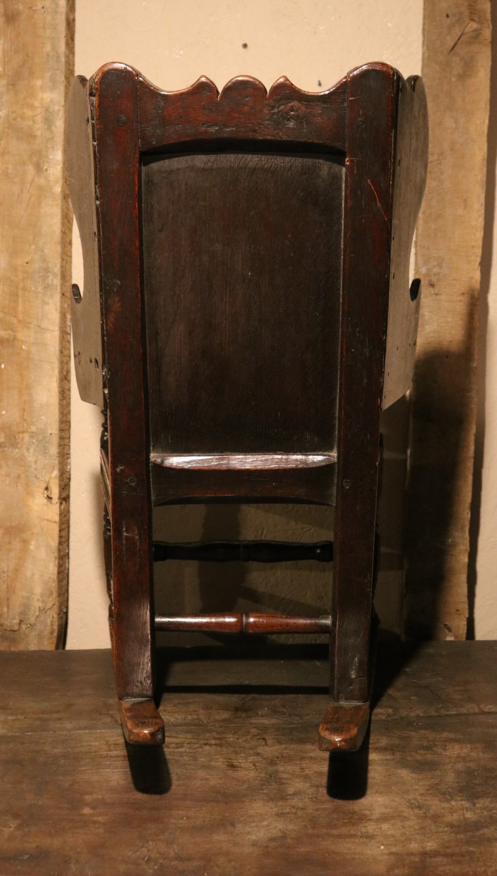 An antique dark oak childs lambing rocking chair featuring shaped winged sides, a panelled backrest, turned front supports, and curved wooden rockers. View X