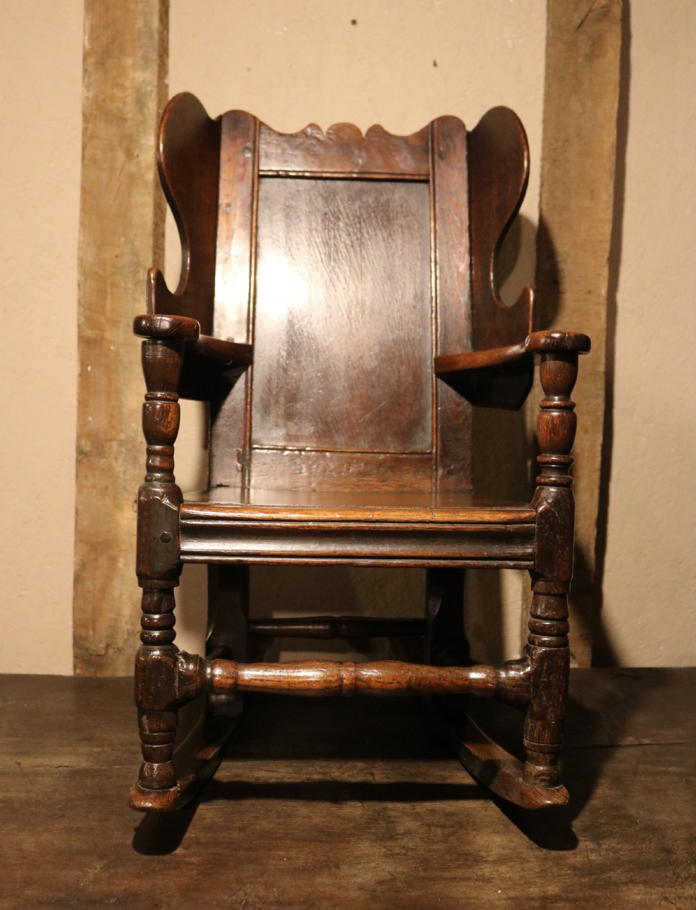 An antique dark oak childs lambing rocking chair featuring shaped winged sides, a panelled backrest, turned front supports, and curved wooden rockers. View XI