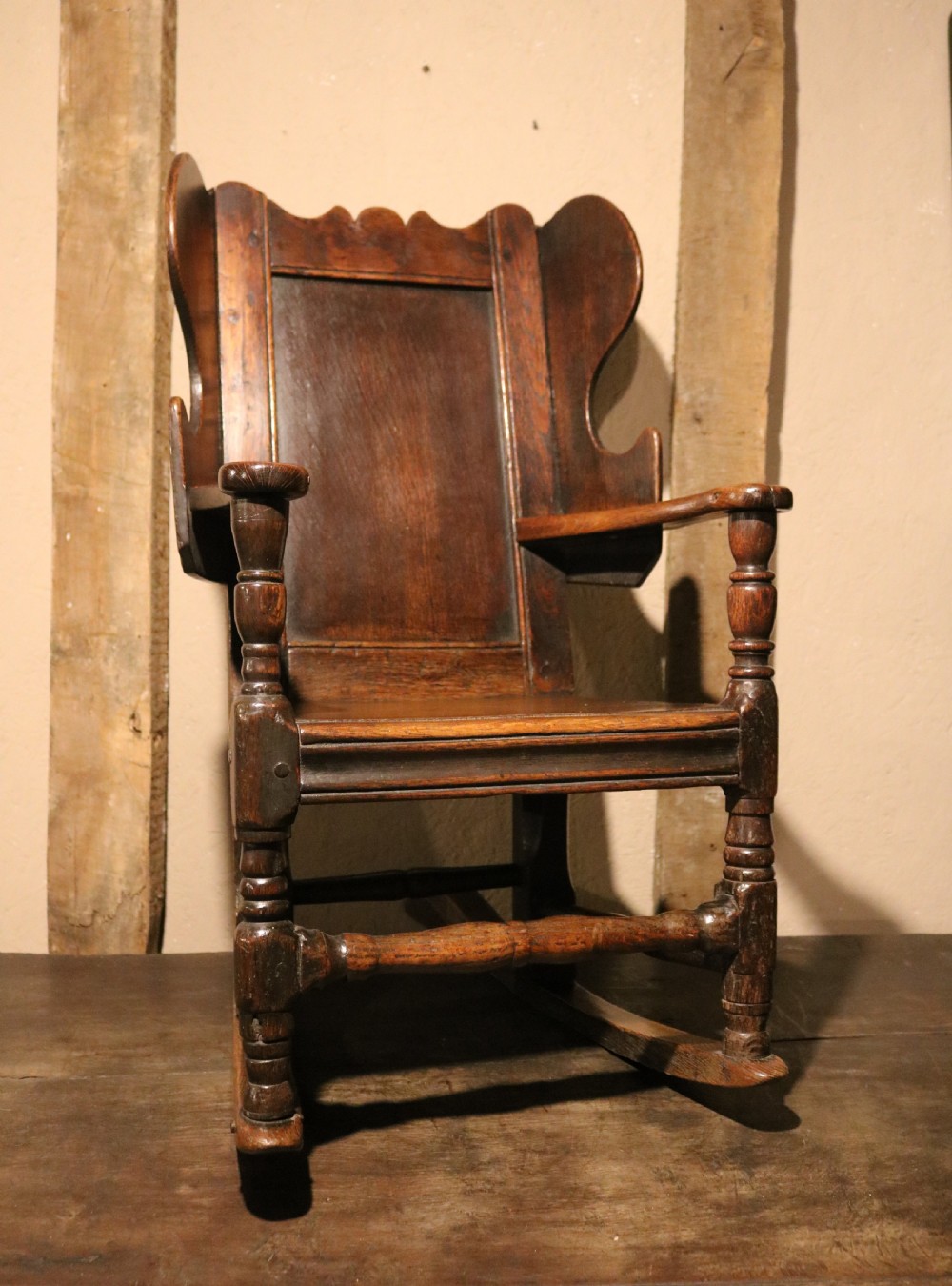 An antique dark oak childs lambing rocking chair featuring shaped winged sides, a panelled backrest, turned front supports, and curved wooden rockers. View XII