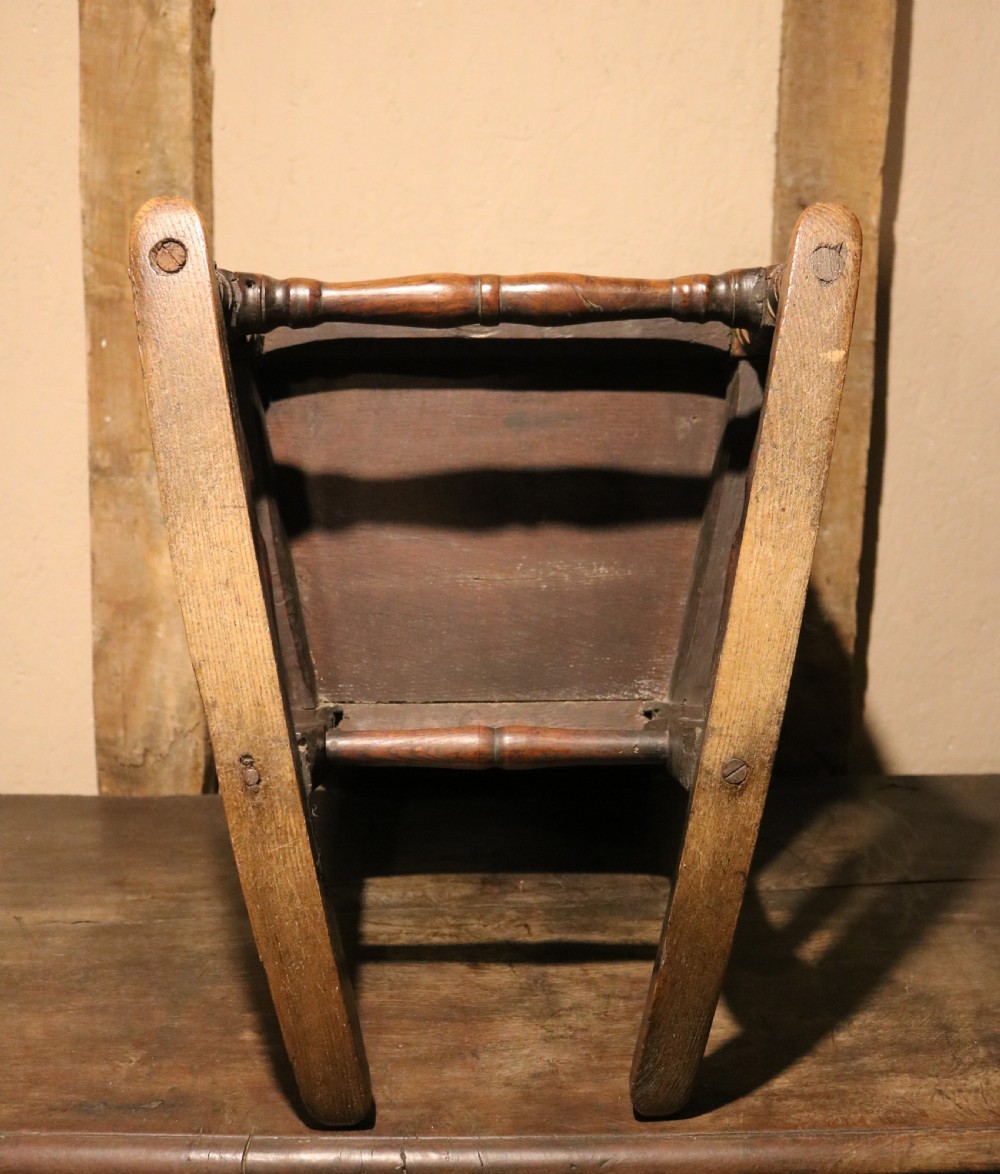 An antique dark oak childs lambing rocking chair featuring shaped winged sides, a panelled backrest, turned front supports, and curved wooden rockers. View XIII