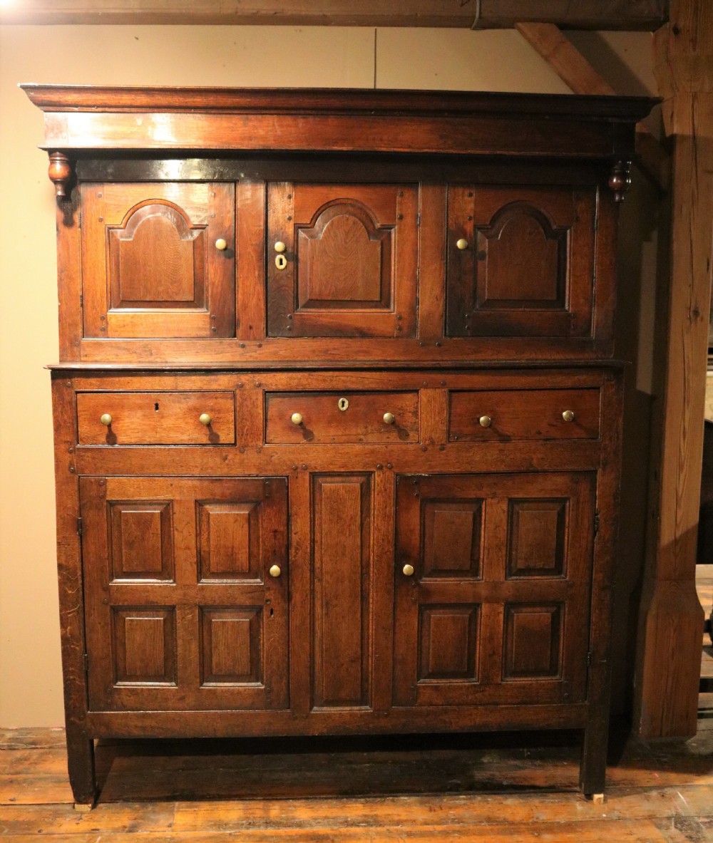 An eighteenth-century Welsh oak deuddarn two-part cupboard featuring a moulded cornice, three upper panelled doors with ogee arches, three mid drawers, and a lower cabinet with field panelled doors.
