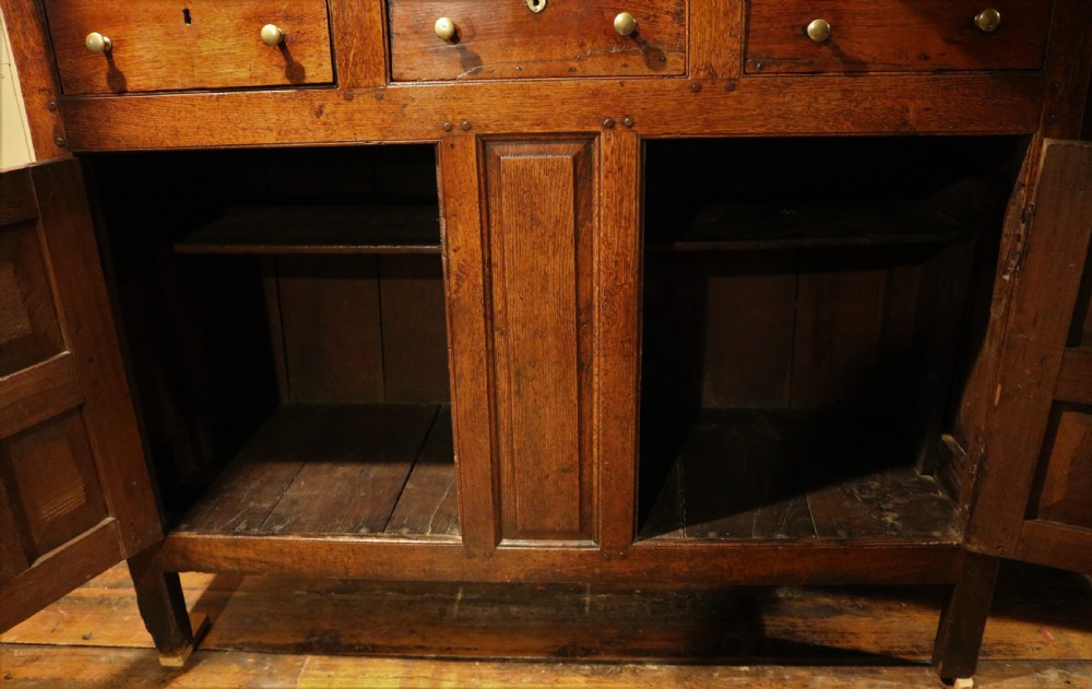 An eighteenth-century Welsh oak deuddarn two-part cupboard featuring a moulded cornice, three upper panelled doors with ogee arches, three mid drawers, and a lower cabinet with field panelled doors. View X