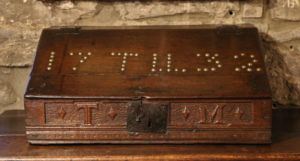 A dark oak sloped desk box featuring brass stud detailing with the year 1732, carved letters T M, and an iron lock plate.