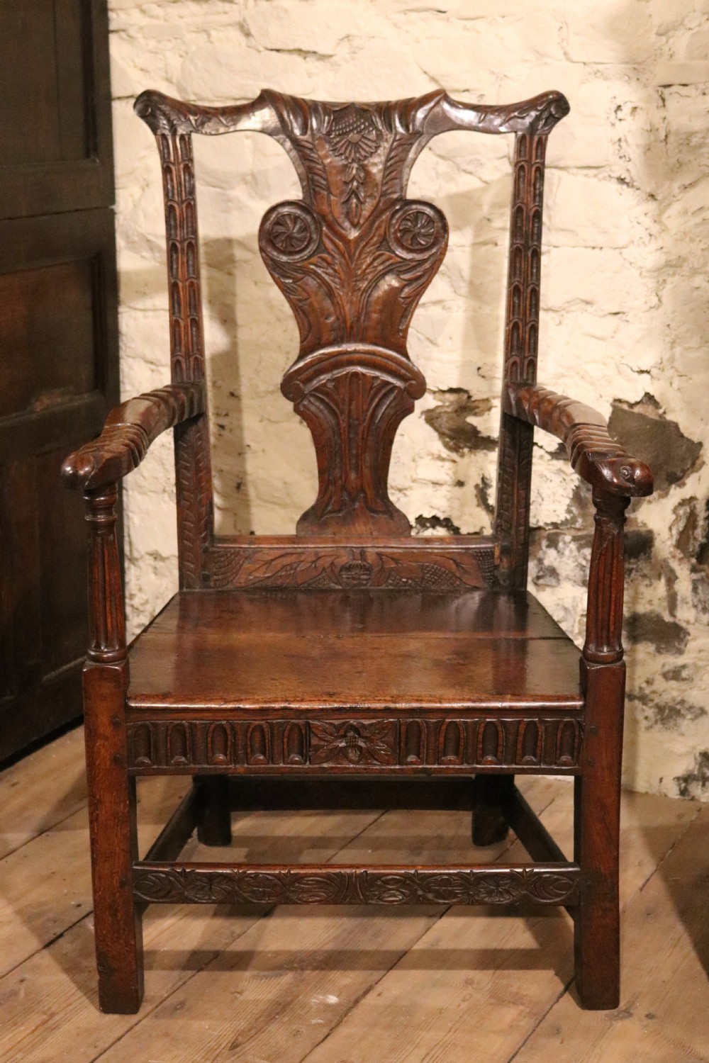 A dark carved oak Welsh armchair dating to the late 18th century with detailed foliate relief carving on the splat back and turned arm supports. View II