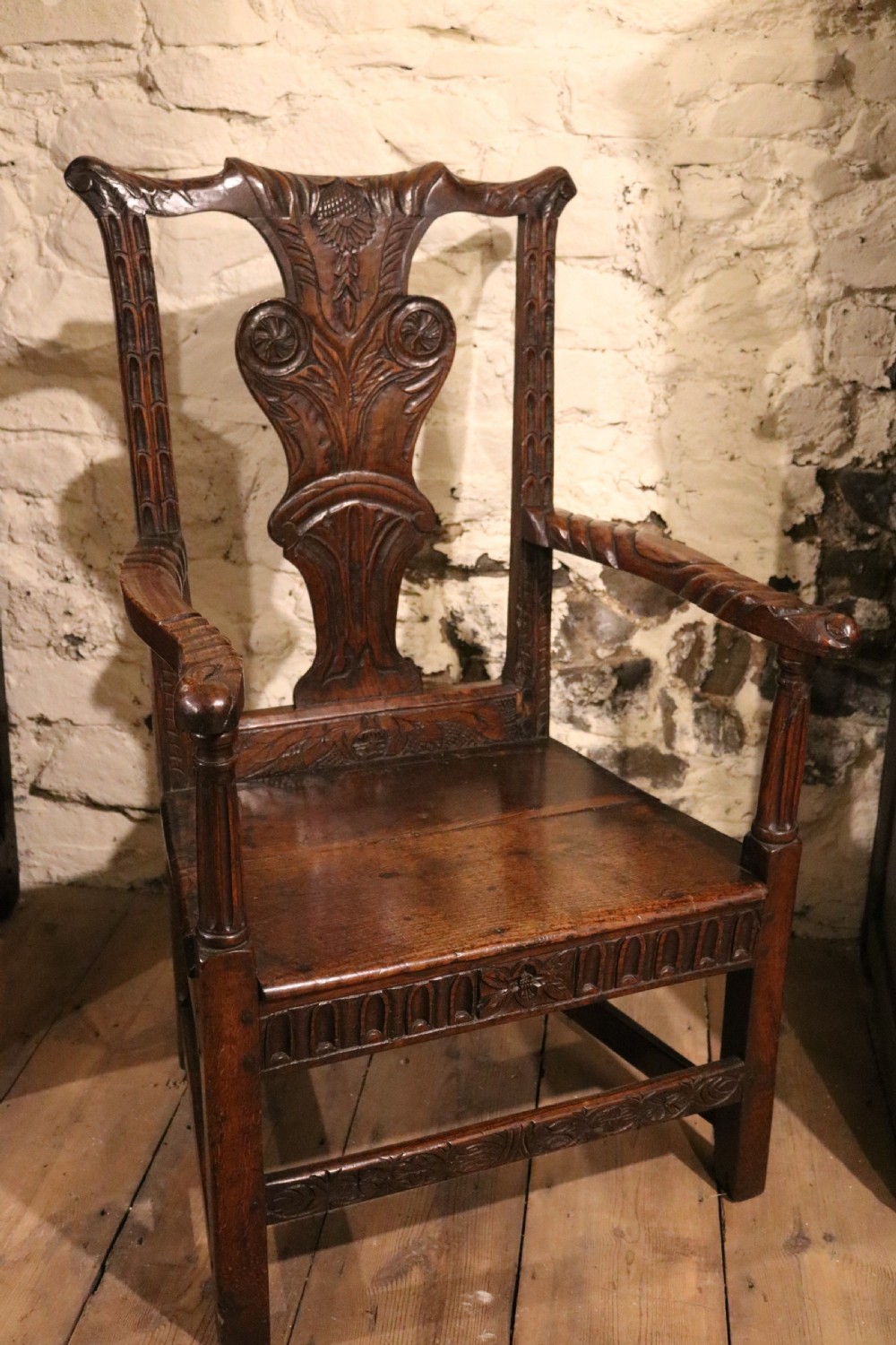 A dark carved oak Welsh armchair dating to the late 18th century with detailed foliate relief carving on the splat back and turned arm supports. View III