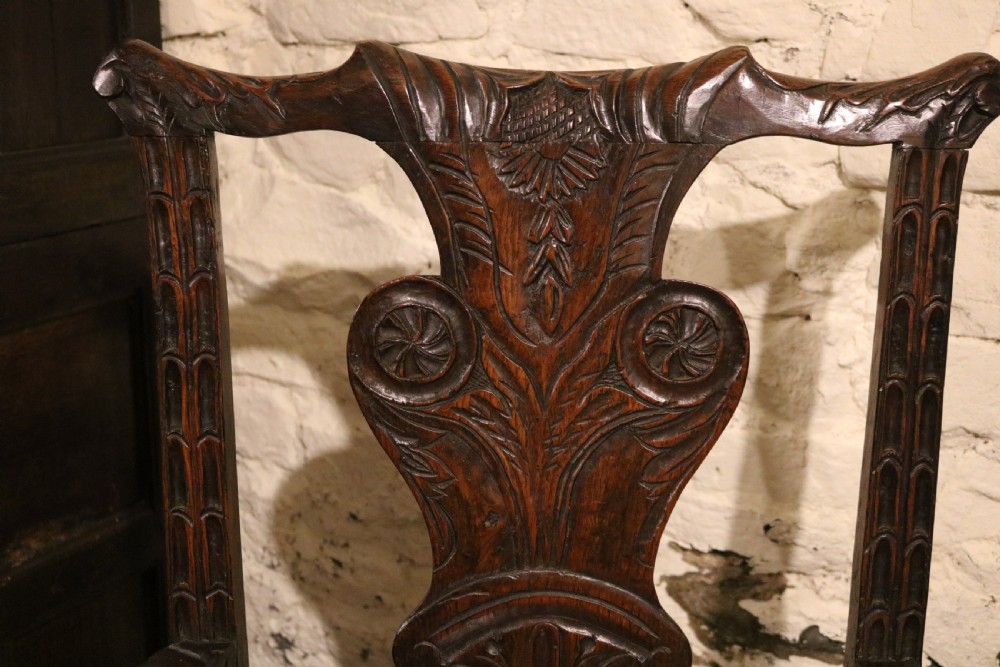A dark carved oak Welsh armchair dating to the late 18th century with detailed foliate relief carving on the splat back and turned arm supports. View X