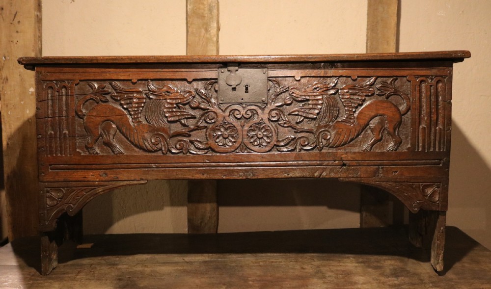 A dark brown carved oak chest featuring relief carvings of dragons, floral rosettes, and a central iron lock plate. View II