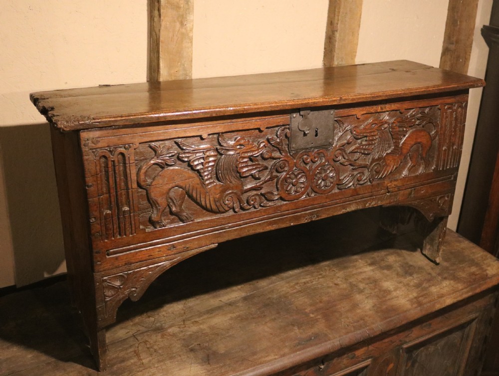 A dark brown carved oak chest featuring relief carvings of dragons, floral rosettes, and a central iron lock plate. View VI