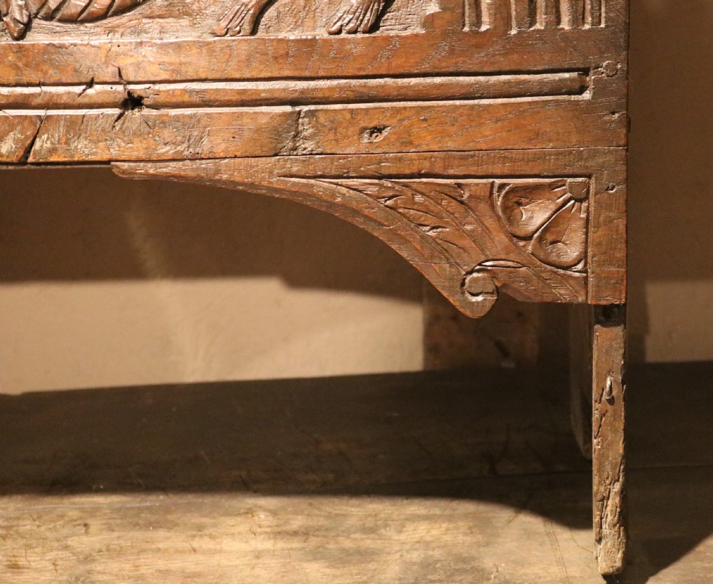 A dark brown carved oak chest featuring relief carvings of dragons, floral rosettes, and a central iron lock plate. View XII