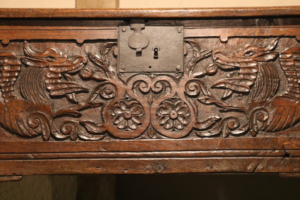A dark brown carved oak chest featuring relief carvings of dragons, floral rosettes, and a central iron lock plate. View XIII