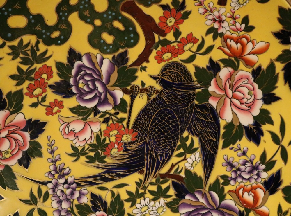 A circular antique ceramic charger with a bright yellow background decorated with colourful hand-painted peony flowers and a bird perched on a branch. View II
