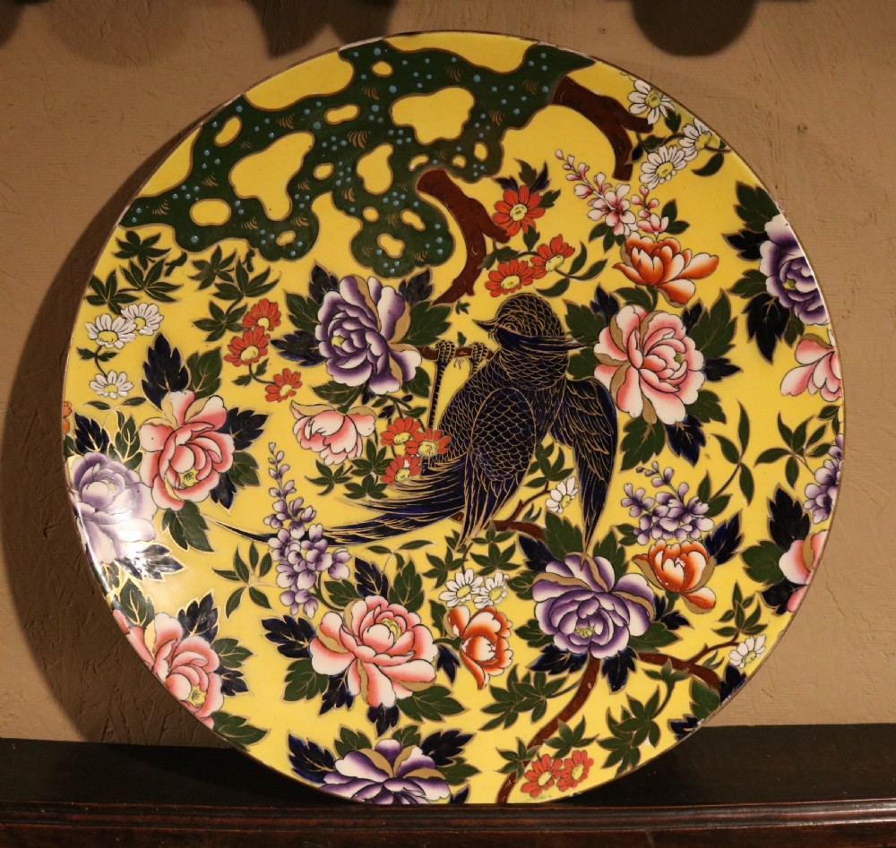 A circular antique ceramic charger with a bright yellow background decorated with colourful hand-painted peony flowers and a bird perched on a branch. View V