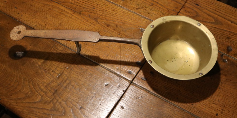 A Georgian brass hearth skillet featuring a rounded brass bowl joined to a long wrought iron handle with an integrated support rest.