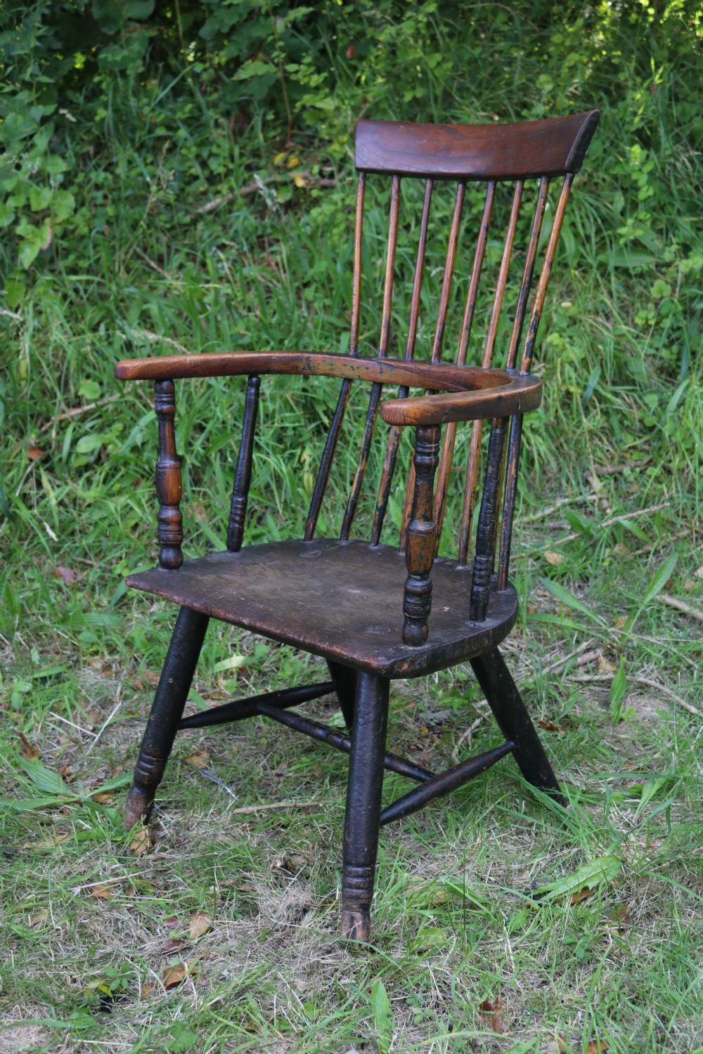 An eighteenth-century Welsh stick chair crafted from dark patinated wood featuring a comb back, curved armrests, and splayed turned legs.