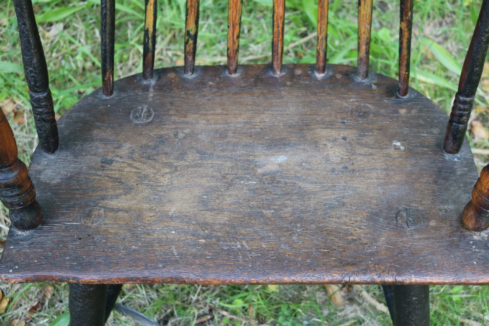 An eighteenth-century Welsh stick chair crafted from dark patinated wood featuring a comb back, curved armrests, and splayed turned legs. View V