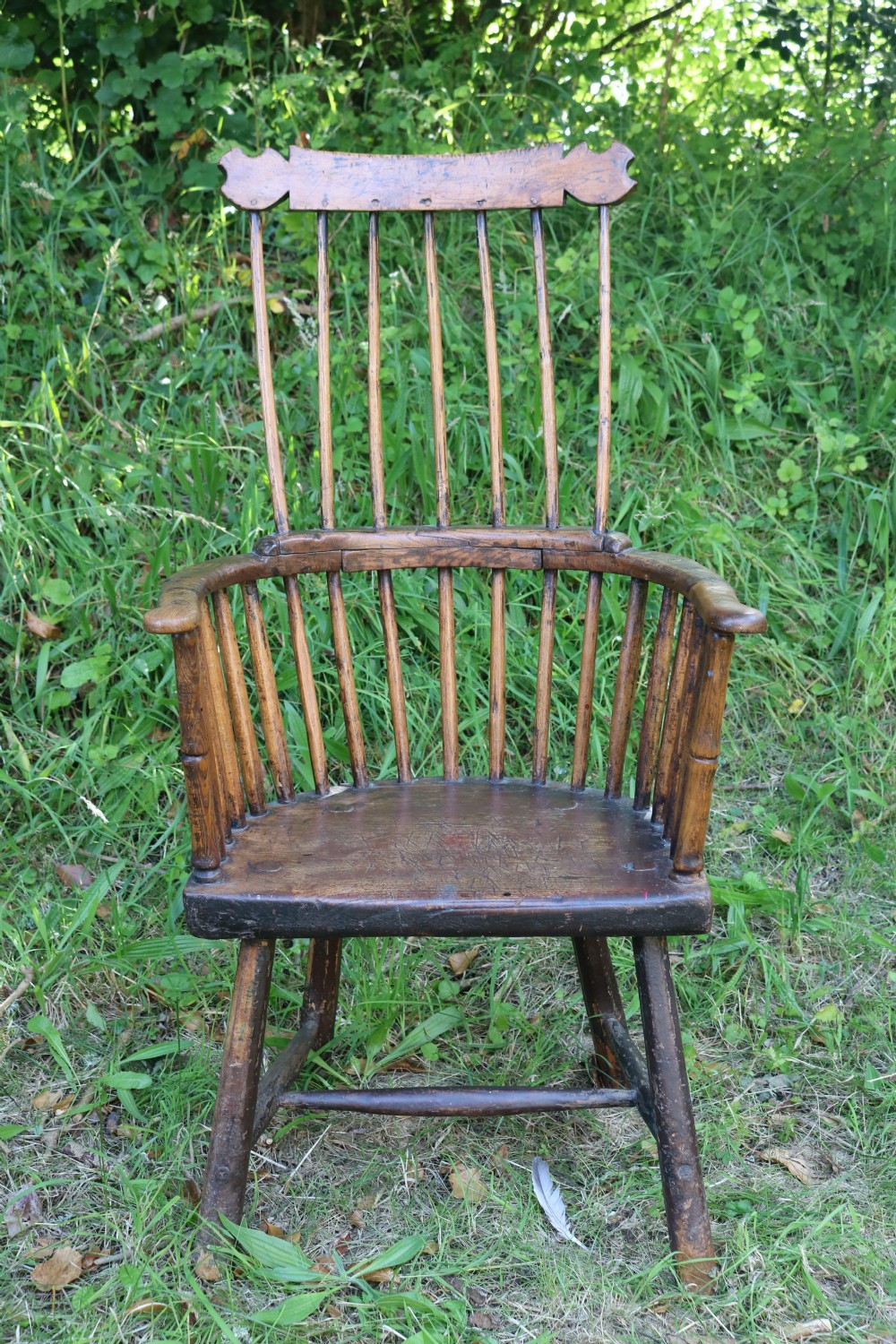 An 18th-century dark oak Welsh stick armchair featuring a shaped comb back, spindle uprights, a solid slab seat, and splayed legs.