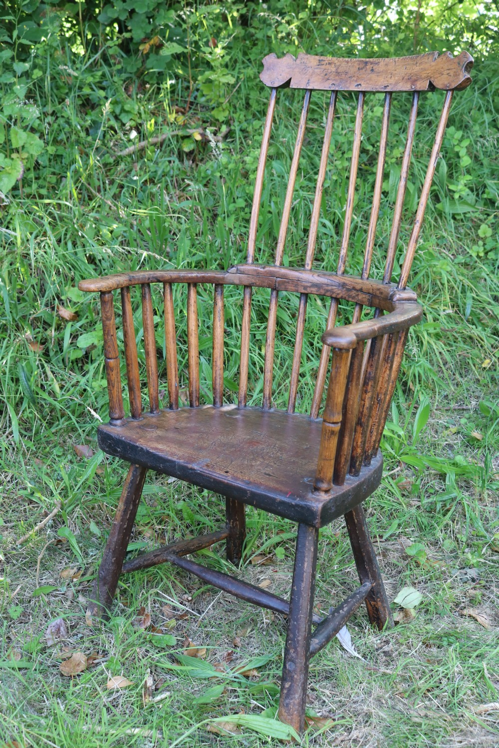 An 18th-century dark oak Welsh stick armchair featuring a shaped comb back, spindle uprights, a solid slab seat, and splayed legs. View II