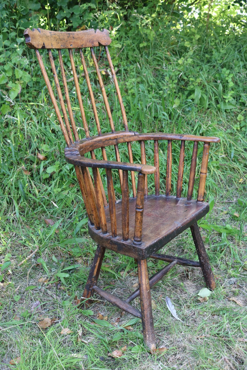 An 18th-century dark oak Welsh stick armchair featuring a shaped comb back, spindle uprights, a solid slab seat, and splayed legs. View III