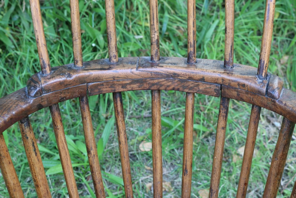 An 18th-century dark oak Welsh stick armchair featuring a shaped comb back, spindle uprights, a solid slab seat, and splayed legs. View X