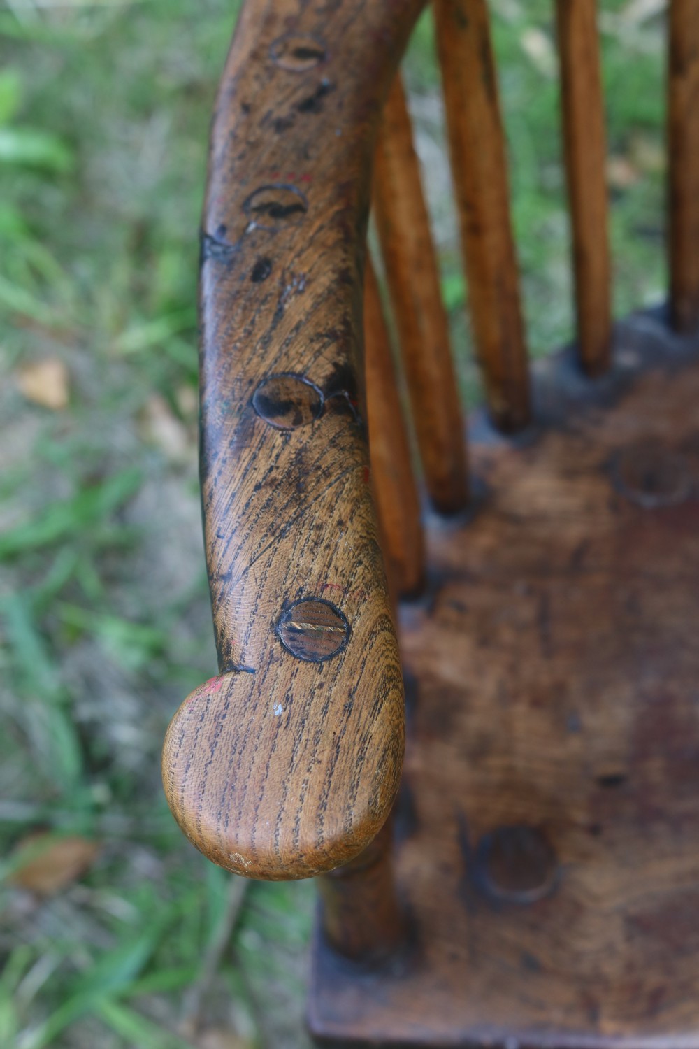 An 18th-century dark oak Welsh stick armchair featuring a shaped comb back, spindle uprights, a solid slab seat, and splayed legs. View XI