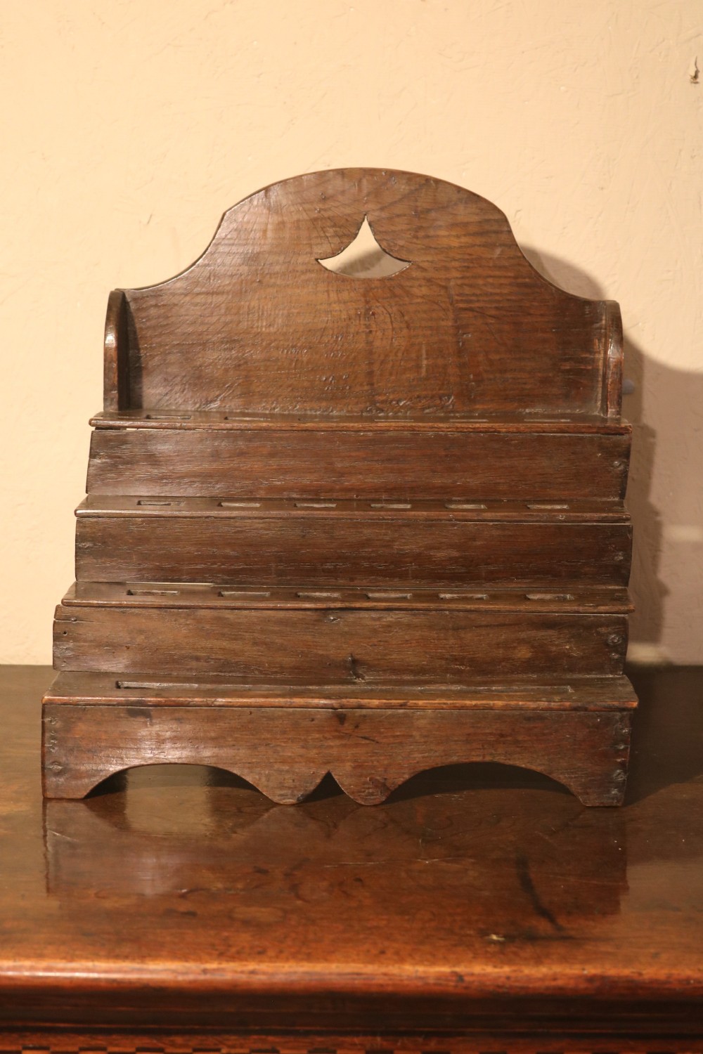 An 18th-century tiered dark oak spoon rack featuring a shaped cresting with a pierced cutout and multiple slotted shelves.