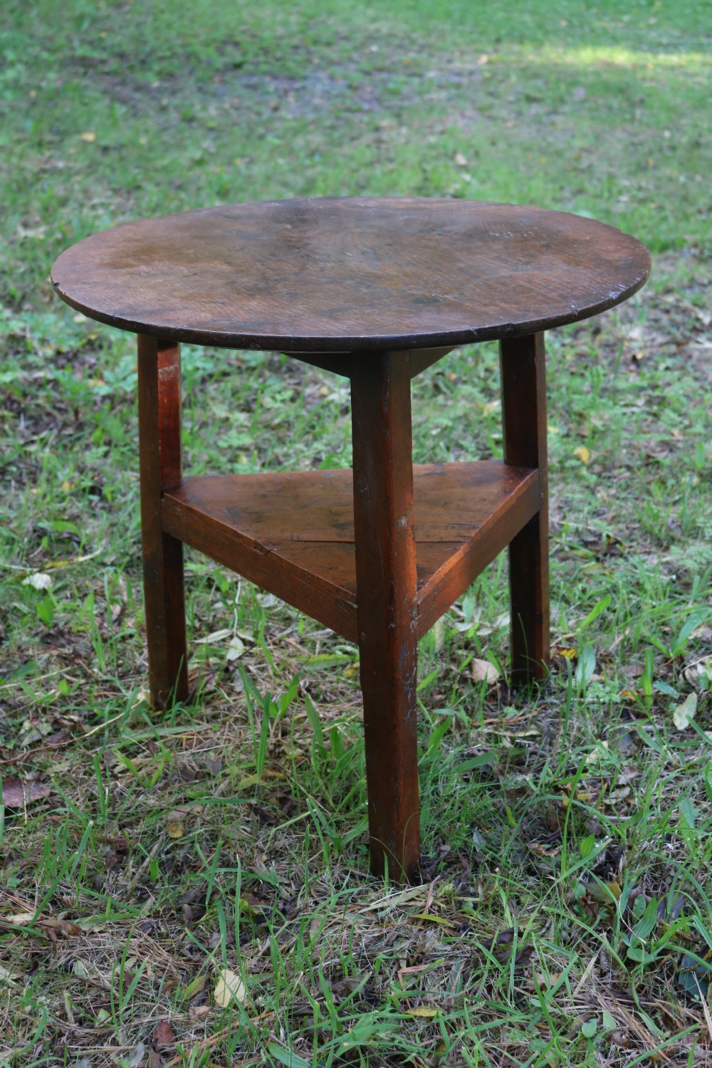 A Georgian three-legged oak cricket table featuring a circular top and a lower triangular stretcher shelf.