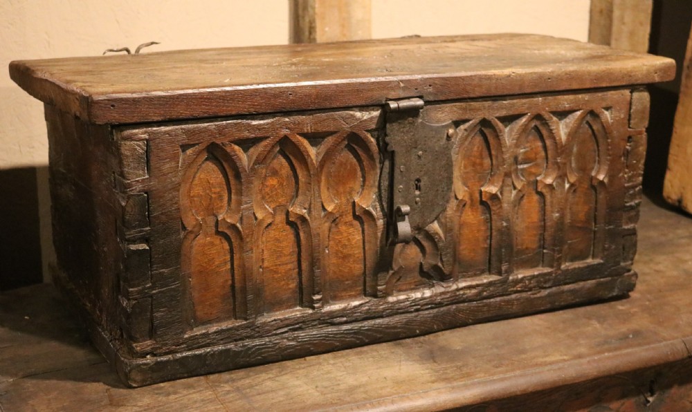 An antique dark brown chestnut wood deed box featuring carved Gothic arch panels and a hand-forged iron lock plate on the front.