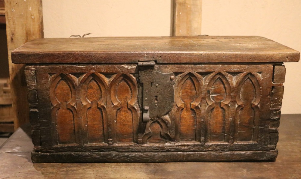 An antique dark brown chestnut wood deed box featuring carved Gothic arch panels and a hand-forged iron lock plate on the front. View V