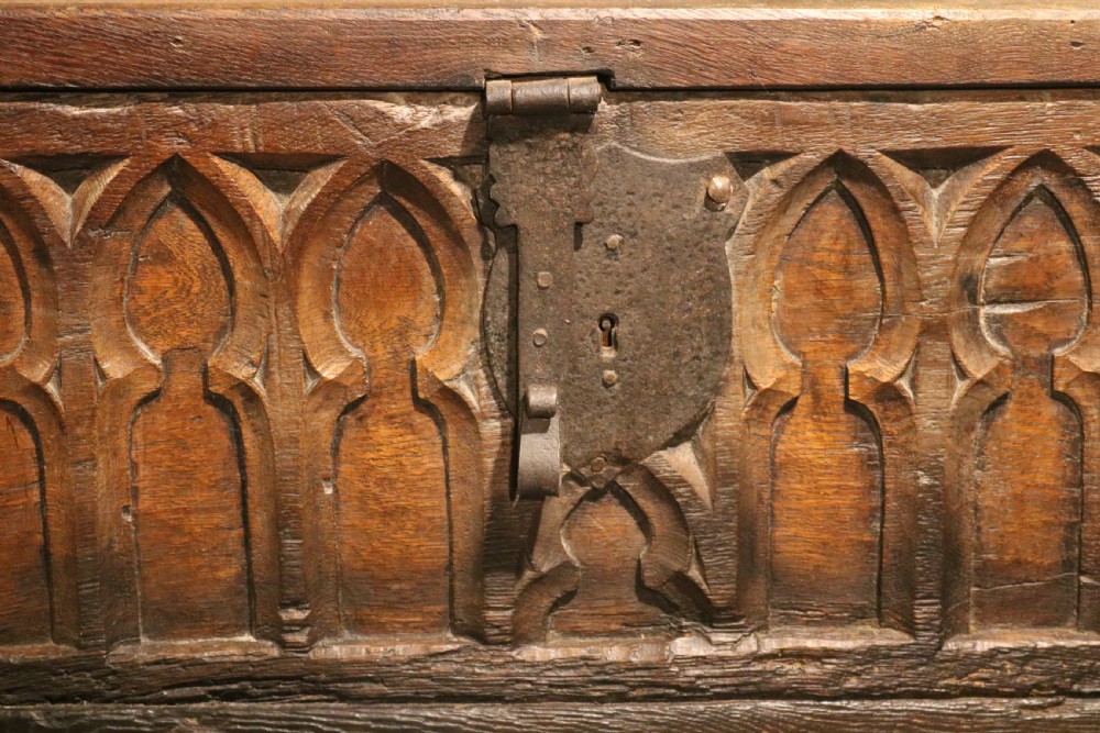 An antique dark brown chestnut wood deed box featuring carved Gothic arch panels and a hand-forged iron lock plate on the front. View VI