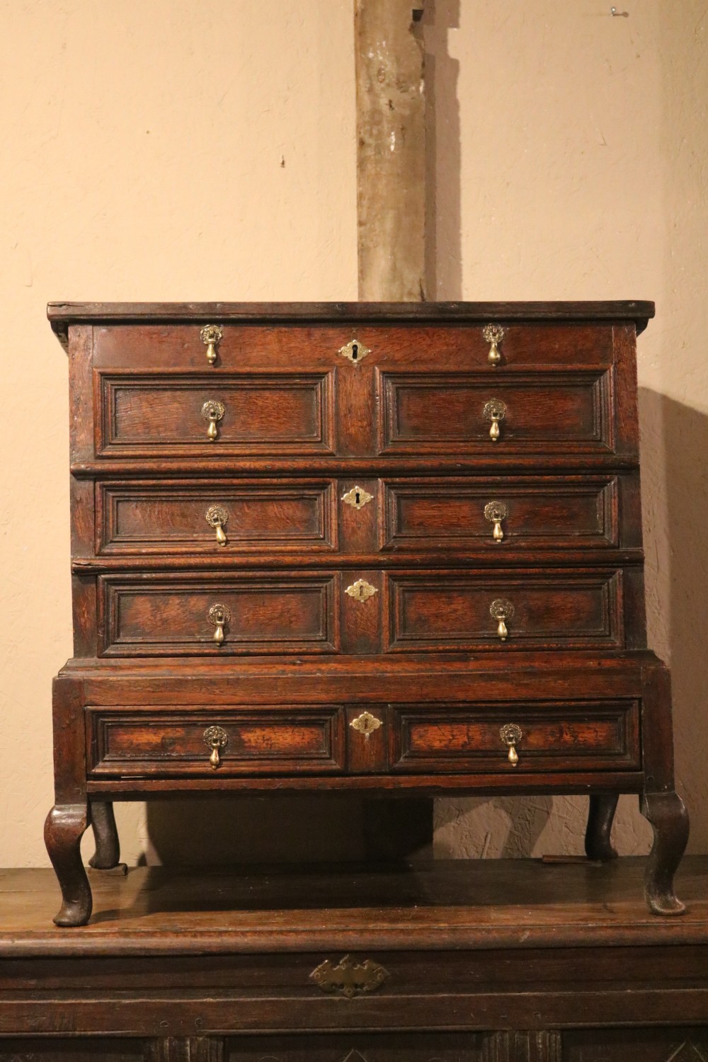 An eighteenth-century dark oak miniature tallboy chest featuring geometric panelled drawer fronts, brass tear-drop handles, and cabriole legs.