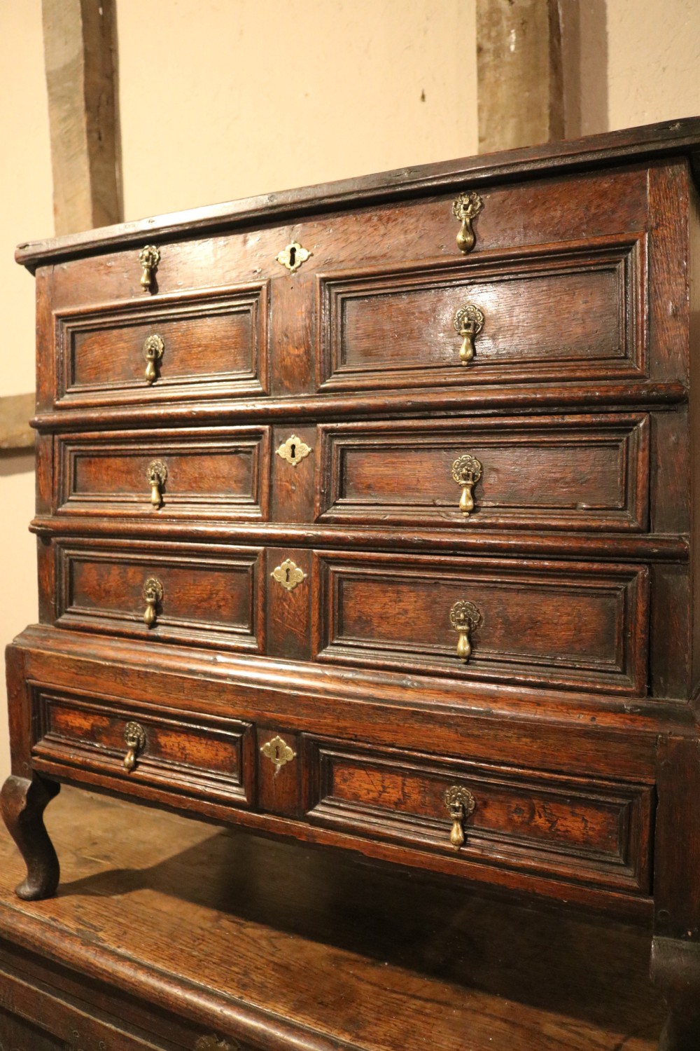 An eighteenth-century dark oak miniature tallboy chest featuring geometric panelled drawer fronts, brass tear-drop handles, and cabriole legs. View IV