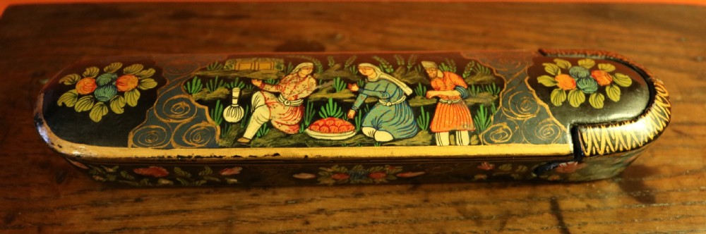 An elongated, rounded antique Indo-Persian lacquered papier-mache pen case featuring hand-painted figures in a landscape with floral end caps. View II