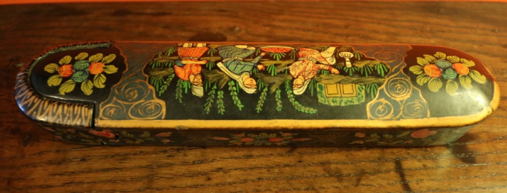An elongated, rounded antique Indo-Persian lacquered papier-mache pen case featuring hand-painted figures in a landscape with floral end caps. View III
