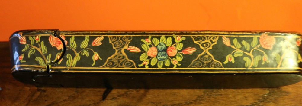 An elongated, rounded antique Indo-Persian lacquered papier-mache pen case featuring hand-painted figures in a landscape with floral end caps. View IV